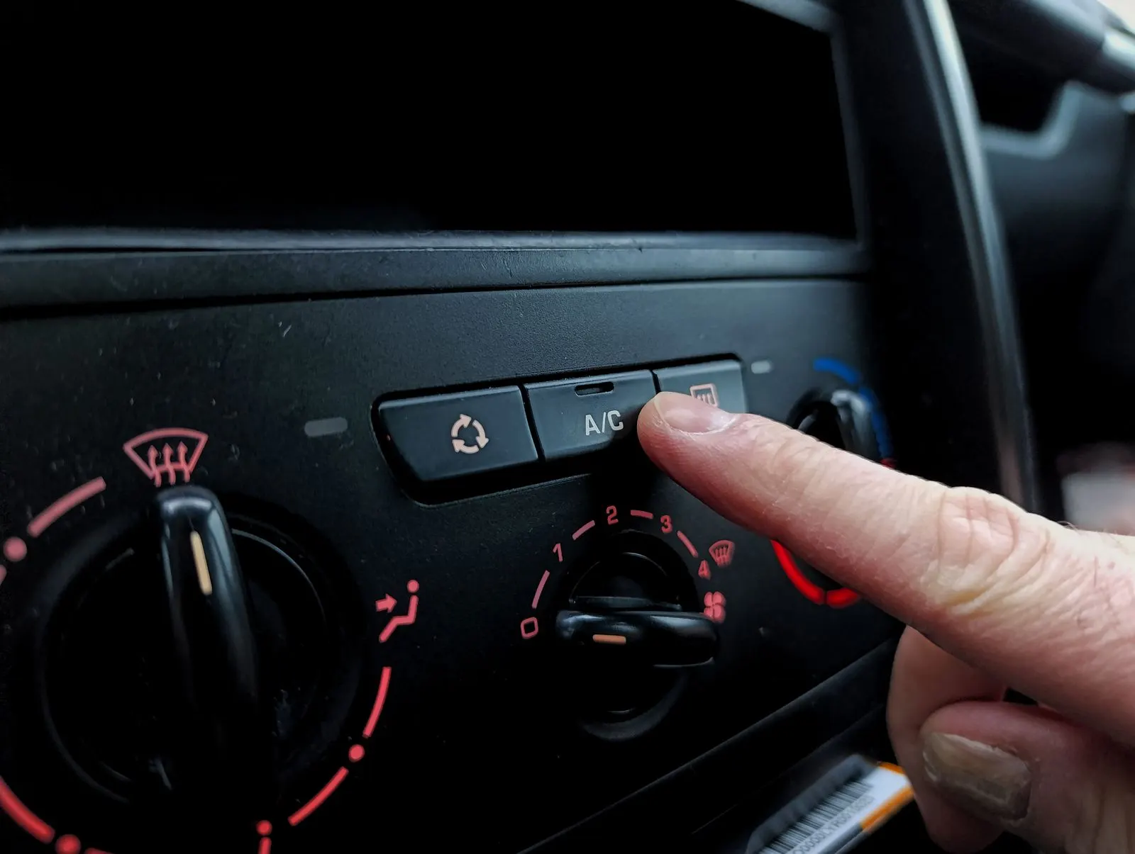 Dedo apertando o botão do ar-condicionado no painel de um carro